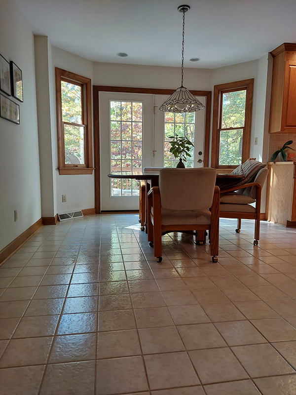 A dining table with chairs sits near large windows and a glass door in a bright, tiled kitchen area.