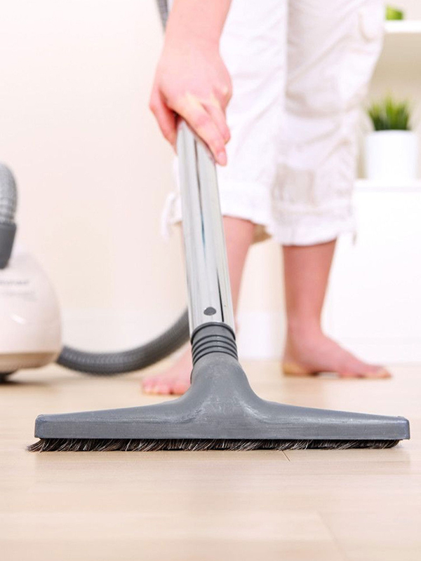 A person using a vacuum cleaner to clean a light-colored floor in a room with minimal decor.