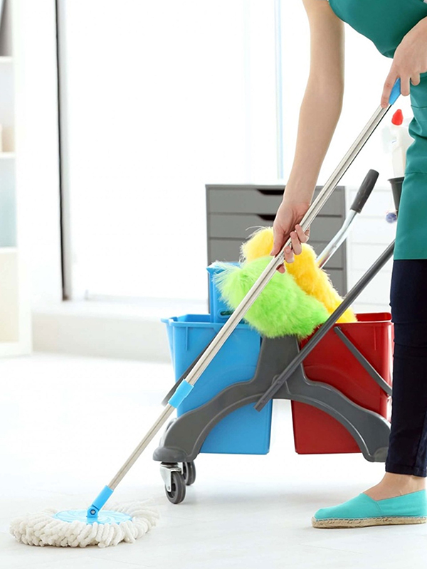 Person mopping a floor with a mop and bucket cart, holding a duster in a bright, clean indoor space.